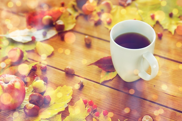 concepto de temporada, bebida y mañana - primer plano de la taza de té en la mesa de madera con hojas de otoño