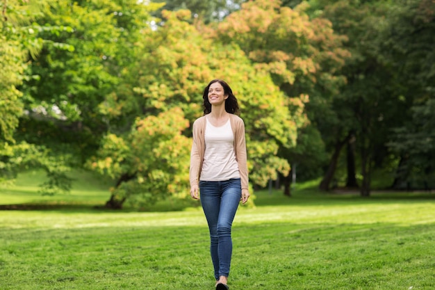 Foto concepto de temporada y gente - hermosa mujer joven feliz caminando en el parque de verano