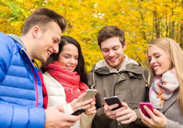 concepto de temporada, gente, tecnología y amistad - grupo de amigos sonrientes con smartphones en el parque de otoño