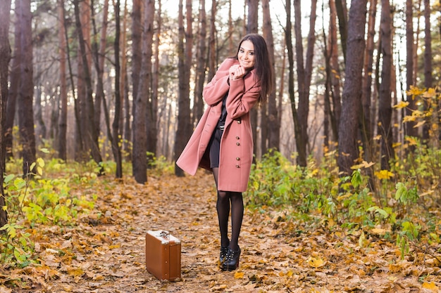 Concepto de temporada, naturaleza y personas - mujer en otoño parque caminando con maleta retro