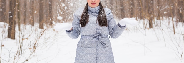 Concepto de temporada, ocio y personas: cerca de la mujer es feliz y tira nieve en la naturaleza invernal