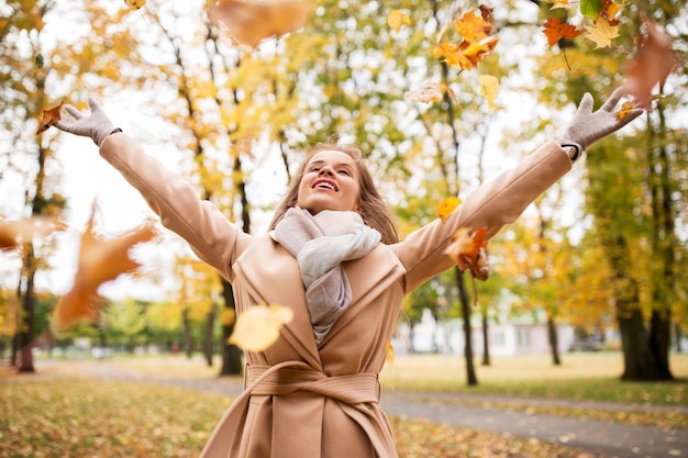 Concepto de temporada y personas - hermosa mujer joven feliz divirtiéndose con hojas en el parque de otoño