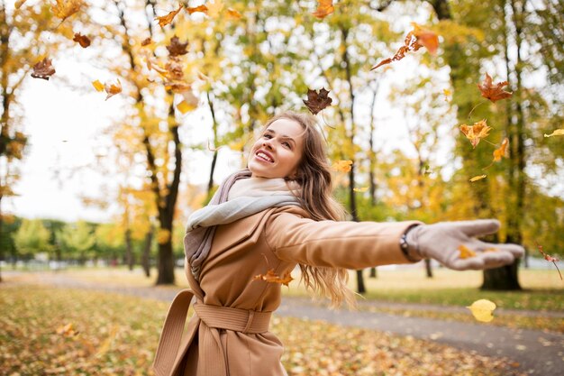 Concepto de temporada y personas - hermosa mujer joven feliz divirtiéndose con hojas en el parque de otoño