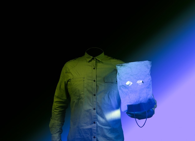 Concepto de terror. El hombre sin cabeza sostiene una bolsa de papel. Ideas de Halloween. Atmósfera espeluznante. Camisa en lugar de persona. Fondo negro.