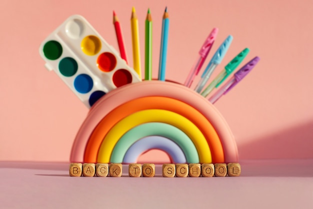 El concepto de tiempo para aprender, diversidad e inclusión. estuche en forma de arco iris brillante con pinturas, lápices, bolígrafos sobre un fondo rosa. inscripción con cubos de madera de regreso a la escuela.