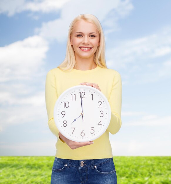 concepto de tiempo, educación y personas - mujer joven sonriente con reloj de pared que muestra 8