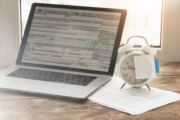 Concepto de tiempo de impuestos. Computadora portátil con formulario de declaraciones de impuestos individuales con post-it en blanco en el despertador