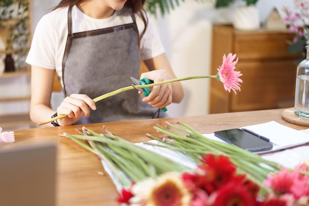 Concepto de tienda de flores Floristería femenina cortando gerbera con tijera para prepararse para hacer un jarrón de flores