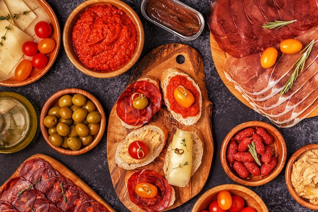 Concepto típico de tapas españolas. El concepto incluye lonchas de jamón, chorizo, salchicha, cuencos con aceitunas, tomates, anchoas, puré de garbanzos, queso.