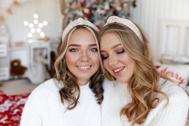 Concepto de tiro de Navidad, dos niñas felices sonrientes amigos gemelos hermanas en el dormitorio junto al árbol