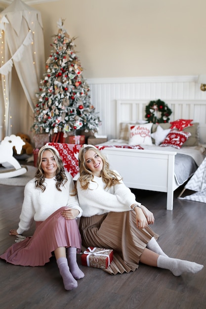 Concepto de tiro de Navidad, dos niñas felices sonrientes amigos gemelos hermanas en el dormitorio junto al árbol