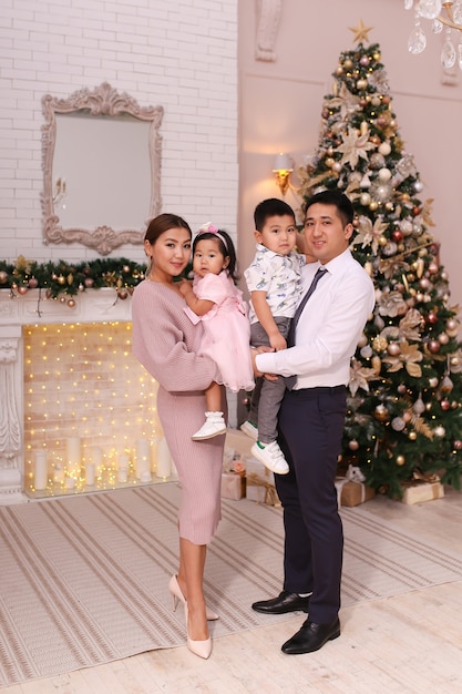 Foto concepto de tiro de navidad, familia asiática con dos niños con ropa elegante está abrazando el árbol