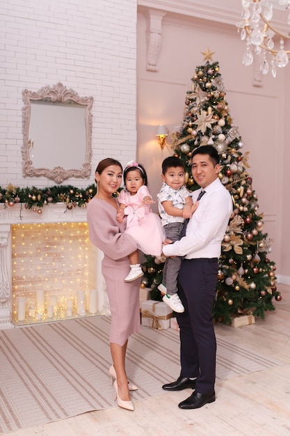 Foto concepto de tiro de navidad, familia asiática con dos niños con ropa elegante está abrazando el árbol