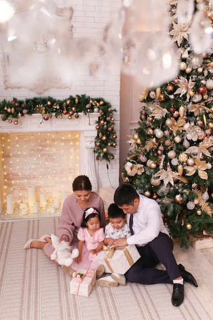 Foto concepto de tiro de navidad, familia asiática con dos niños con ropa elegante está abrazando el árbol