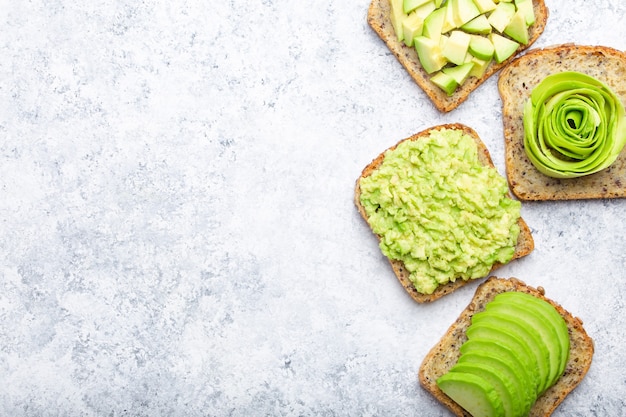 Concepto de tostadas de desayuno saludable con aguacate aplastado, rodajas, trozos y rosa. Diferentes formas de hacer y servir un delicioso sándwich de aguacate, vista superior, fondo blanco, primer plano. Espacio para texto