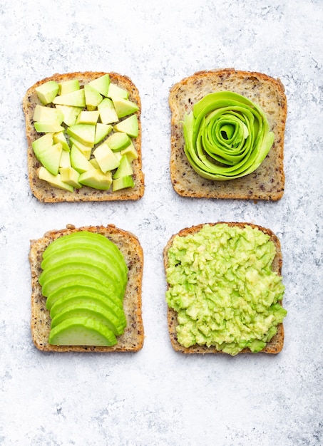 Concepto de tostadas de desayuno saludable con aguacate aplastado, rodajas, trozos y rosa. Diferentes formas de preparar y servir un delicioso sándwich de aguacate, vista superior, fondo de piedra blanca, primer plano