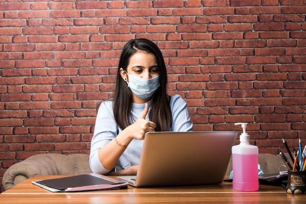 Concepto de trabajo de coronavirus desde el hogar - Cuarentena de mujer de negocios bonita india, trabajando en una computadora portátil con una mascarilla médica protectora