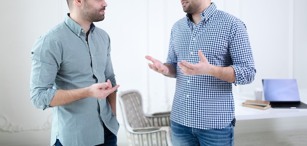 Concepto de trabajo en equipo empresarial. Primer plano de las manos de dos hombres de negocios hablando en la oficina. Ordenador portátil, café y cuaderno de mesa blanca.