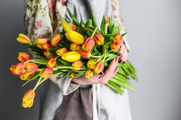 El concepto del trabajo del florista. Una niña sostiene un ramo de tulipanes amarillos, naranjas y rojos. Fondo blanco