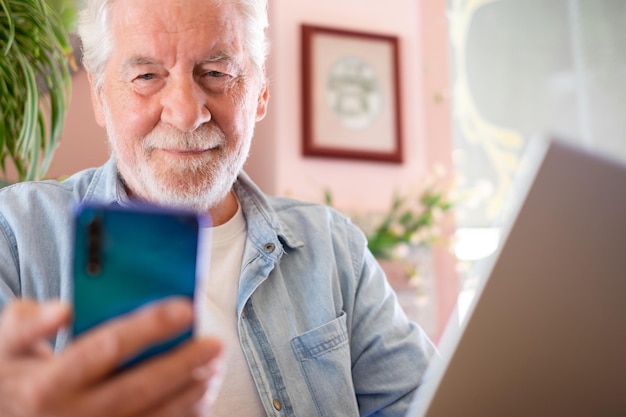 Concepto de trabajo inteligente Hombre senior sonriente en una cafetería mientras trabaja en una computadora portátil usando un teléfono móvil