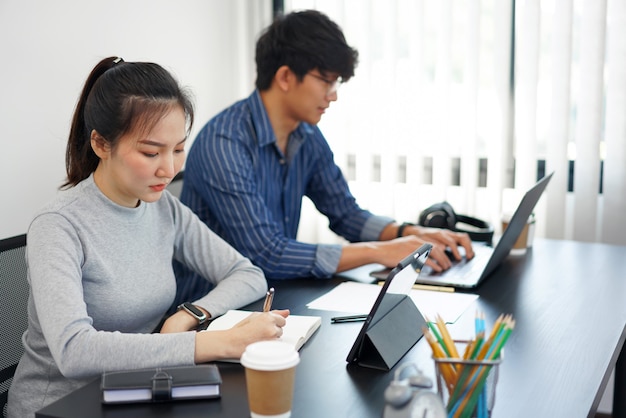 Concepto de trabajo de oficina dos personas de negocios que trabajan en los dispositivos con dos tazas de café en la oficina.