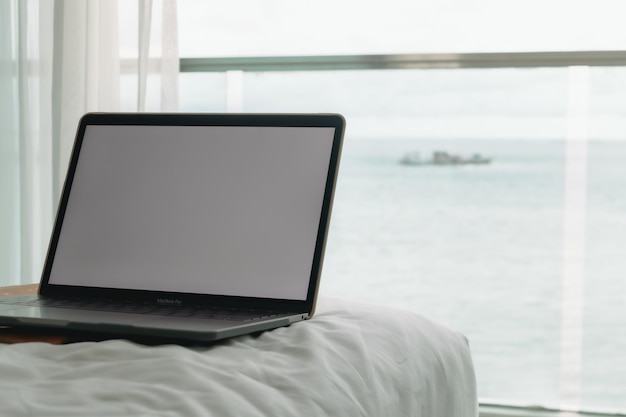 Concepto de trabajo portátil con pantalla vacía en la cama y balcón con vista al mar