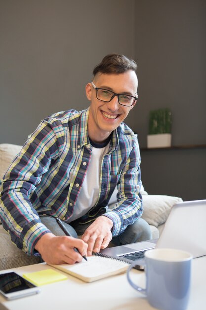 Concepto de trabajo remoto, oficina en casa. Cerrar vista de joven sonriente trabajando en forma independiente fuera de la oficina