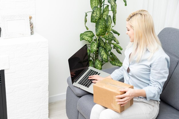 Concepto de transporte, correos y personas - mujer joven sonriente abriendo una caja de cartón en casa