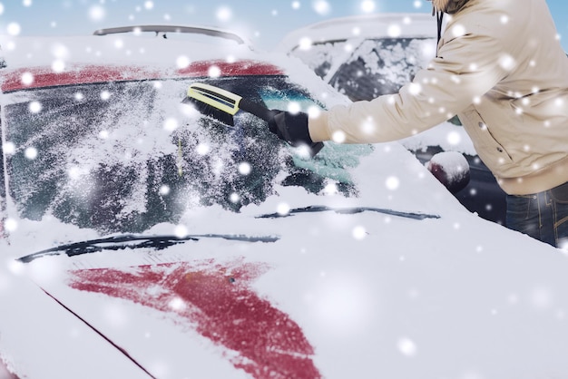 concepto de transporte, invierno, personas y vehículos - cierre del hombre limpiando la nieve del parabrisas del camión con cepillo