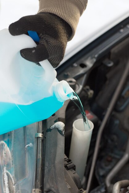 concepto de transporte, invierno y vehículo - cierre del hombre vertiendo anticongelante en el tanque de agua del parabrisas