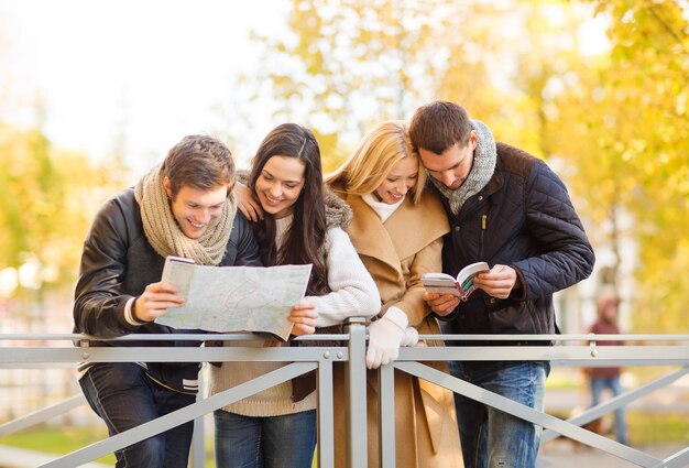 Concepto de turismo y vacaciones - grupo de amigos o parejas con mapa turístico en el parque de otoño