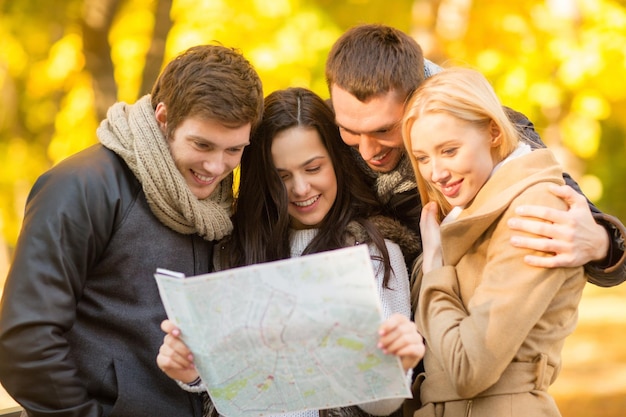 Concepto de turismo y vacaciones - grupo de amigos o parejas con mapa turístico en el parque de otoño