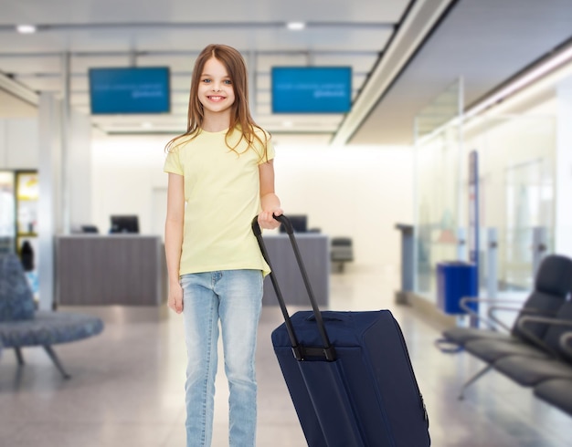 concepto de turismo, vacaciones, vacaciones, infancia y transporte - niña sonriente con bolsa de viaje sobre el fondo del aeropuerto