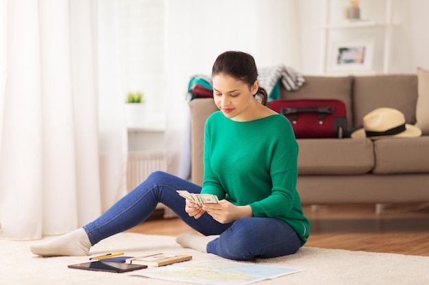 concepto de turismo, viajes, finanzas y personas - mujer joven feliz con dinero, computadora de tablet pc y mapa en casa