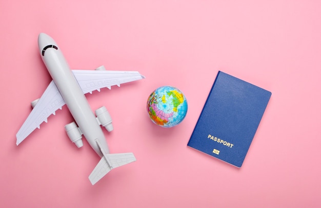 Concepto de turismo y viajes. Globo, pasaporte, figura de avión de pasajeros en la pared rosa pastel Vista superior. Endecha plana