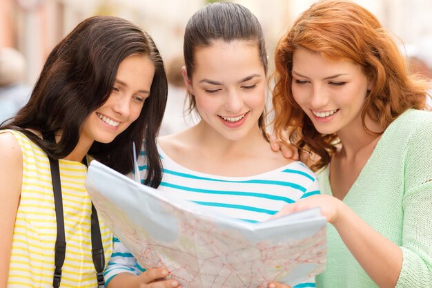 concepto de turismo, viajes, ocio, vacaciones y amistad - adolescentes sonrientes con mapa y cámara al aire libre