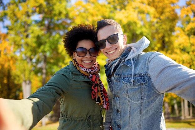 concepto de turismo, viajes, personas, temporada y tecnología - feliz pareja internacional de adolescentes tomando selfie sobre el fondo del parque de otoño