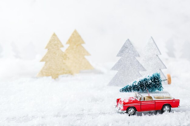 Concepto de vacaciones de año nuevo Coche de juguete rojo con árbol de Navidad en un bosque nevado Tarjeta de felicitación de espacio de copia con decoración festiva