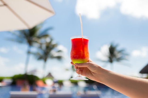 concepto de vacaciones, bebidas y viajes - primer plano de la mano femenina sosteniendo un vaso con cóctel