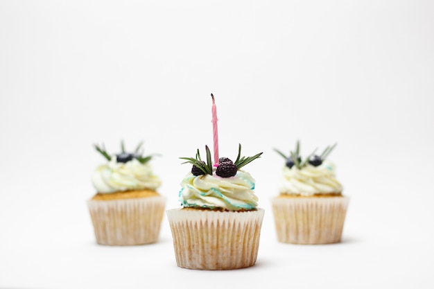 Foto concepto de vacaciones, celebración, saludo y fiesta - cumpleaños tres cupcake con velas encendidas sobre una superficie blanca