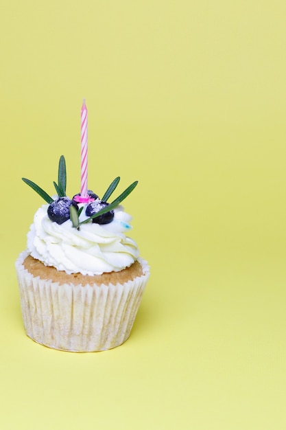 Concepto de vacaciones, celebración, saludo y fiesta - cupcake de cumpleaños con velas encendidas sobre fondo amarillo