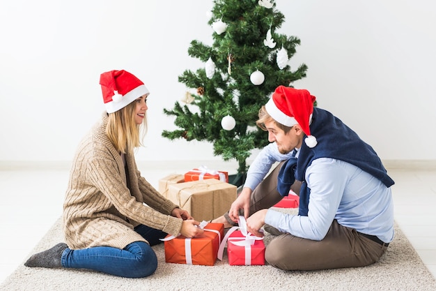 Concepto de vacaciones - dulce pareja abriendo regalos de Navidad, sentado en la sala de estar