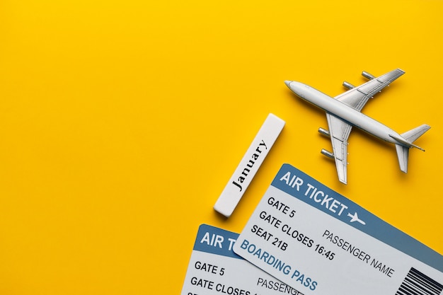Concepto de vacaciones de enero con avión y entradas sobre fondo amarillo con espacio de copia y vista superior.