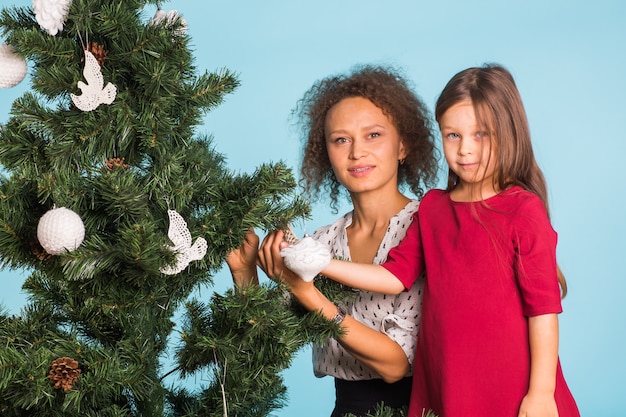 Concepto de vacaciones, familia y Navidad - madre e hija de raza mixta decorando el árbol de Navidad en