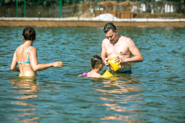 Concepto de vacaciones familiares joven mamá con papá enseñando a nadar a su hijo