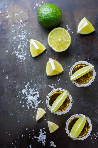 Concepto de vacaciones de fiesta de comida chatarra con alcohol Tequila mexicano dorado disparado en una mesa negra grunge con sal y lima Copiar espacio fondo vista superior plana sobre la cabeza