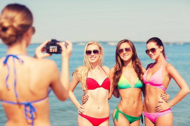 Foto concepto de vacaciones, gestos, viajes y personas de verano - grupo de mujeres jóvenes sonrientes fotografiando por cámara y agitando las manos en la playa