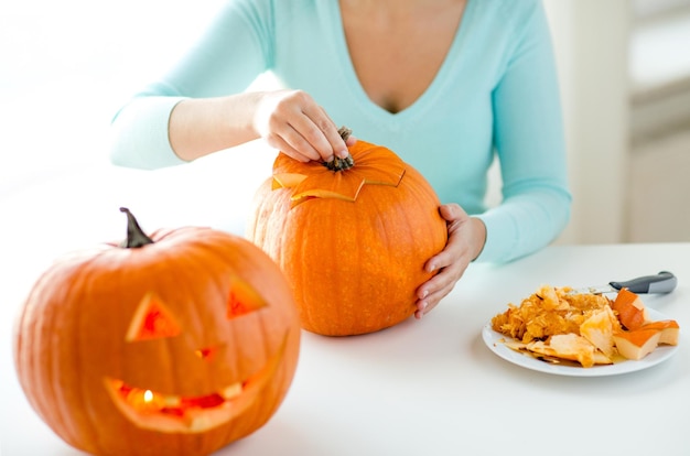 Concepto de vacaciones, halloween, decoración y personas - cerca de mujer con calabazas en casa