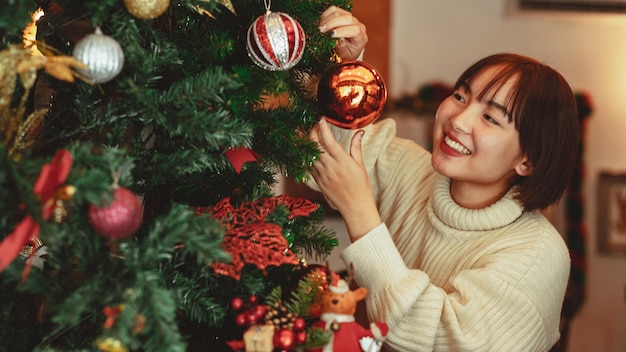 Concepto de vacaciones de invierno, mujer feliz decorando el árbol de Navidad para la celebración del año nuevo.