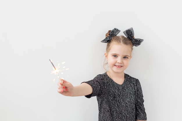 Concepto de vacaciones, Navidad y año nuevo - Niño feliz tiene bengala ardiente en su mano sobre fondo blanco con espacio de copia.